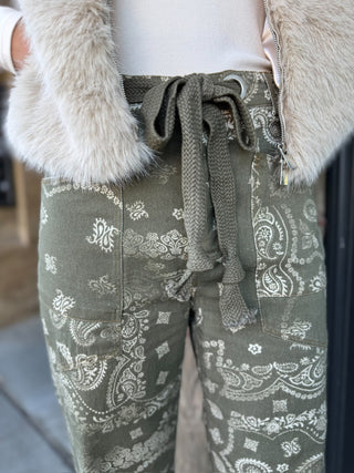 Olive green pants with a white paisley bandana print and a matching knotted drawstring waist, styled with a cream zip jacket and faux fur trim.