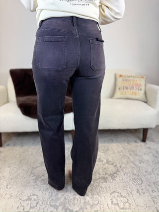 A person shown from the back wearing dark charcoal gray wide-leg jeans in a living room setting with a white sofa and patterned rug.