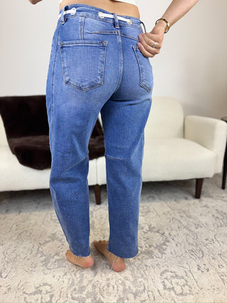 A person shown from the back wearing medium-wash blue jeans in a living room setting with a white sofa and patterned rug.