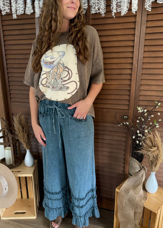 Person wearing a graphic t-shirt and blue jeans standing in front of wooden shutters.
