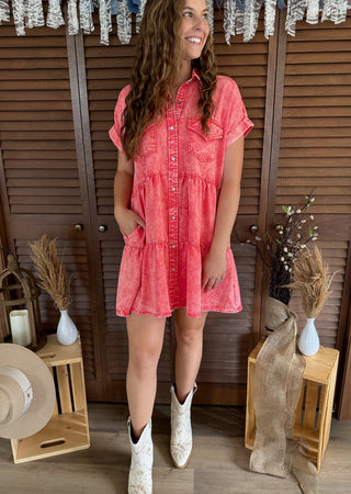 Woman wearing a pink dress and white boots standing in a rustic setting with wooden shutters and decor.