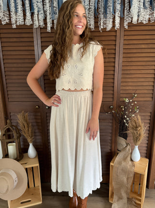 Woman wearing a white dress standing in front of wooden shutters with decorative elements.