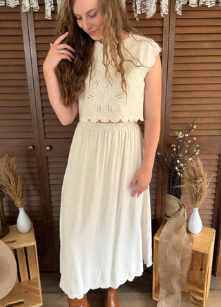 Woman wearing a beige lace dress standing in front of wooden shutters.