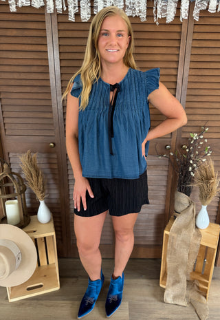 Woman wearing a blue top and black shorts standing in front of a wooden background with decorative elements.
