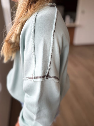 Light blue denim shirt with frayed edges worn by a person, blurred background