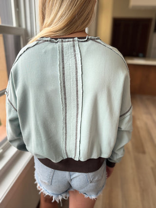 Light green jacket with brown accents worn by a person, standing indoors.