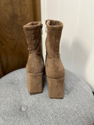Pair of brown suede platform boots on a textured surface with a neutral background