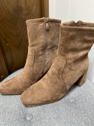 Pair of brown suede ankle boots on a textured surface with a wooden background.