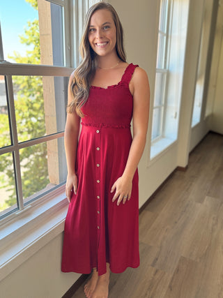 Woman in a red dress standing by a window in a well-lit room.