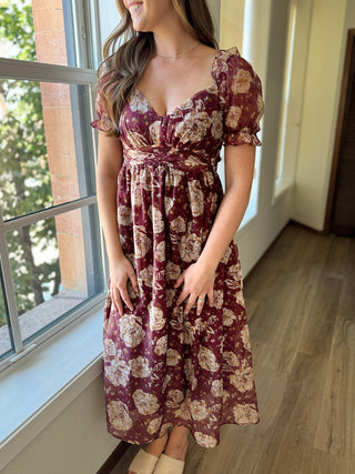 Woman wearing a floral dress standing by a window indoors