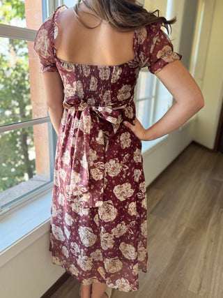 Person wearing a floral dress standing by a window