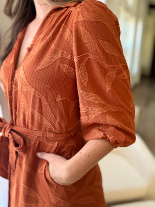 Person wearing a rust-colored dress with leaf pattern