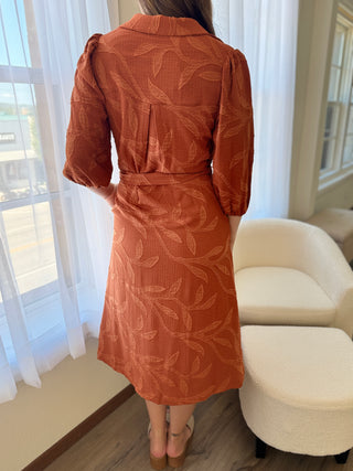 Person wearing a rust-colored dress with leaf pattern in a bright room.