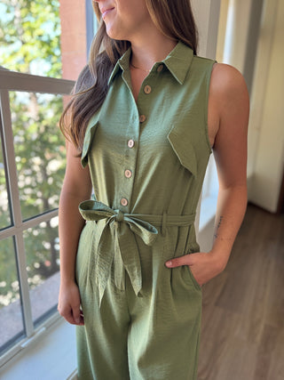 Woman wearing a green jumpsuit standing indoors with a window in the background