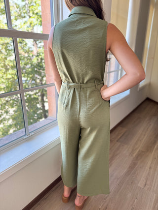 Person wearing a green jumpsuit standing by a window with a view of trees.