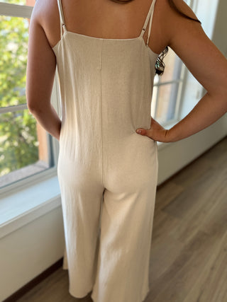 Person wearing a beige jumpsuit standing indoors with a window in the background