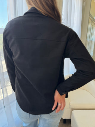 Person wearing a black jacket in an indoor setting with light-colored walls and furniture.