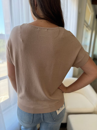 Person wearing a beige t-shirt with 'NUNU' branding, standing indoors.