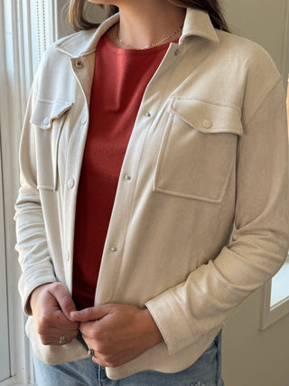 Person wearing a beige jacket over a white shirt with a red garment underneath, standing indoors.