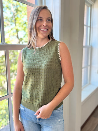 Woman wearing a green sleeveless crochet top standing by a window with natural light.