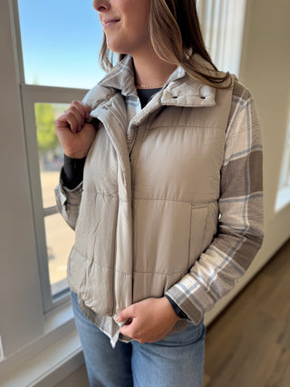 Person wearing a beige puffer vest over a plaid shirt indoors.