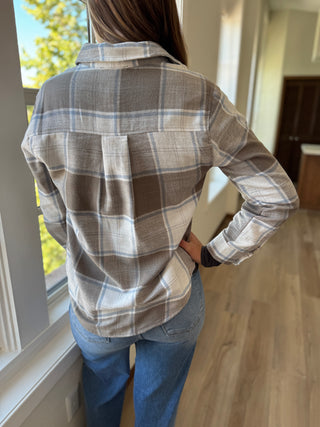 Person wearing a plaid shirt and jeans standing in a room with a window.