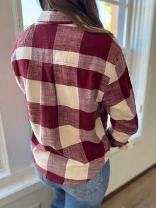 Person wearing a red and white checkered shirt with blue jeans indoors.