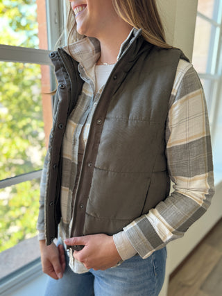 Person wearing a brown vest over a plaid shirt indoors