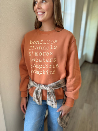 Person wearing a brown sweatshirt with autumn-themed text, standing indoors.