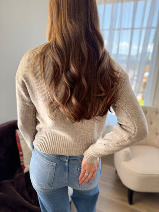 Person wearing a beige sweater and blue jeans in a room with a window in the background