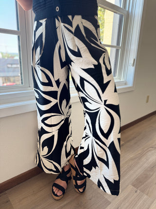 Person wearing black and white patterned pants standing in a room with a window.