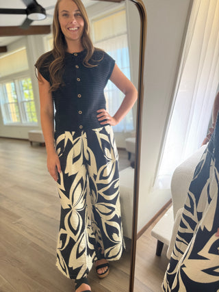 Woman wearing a navy dress with white leaf patterns standing in front of a full-length mirror.