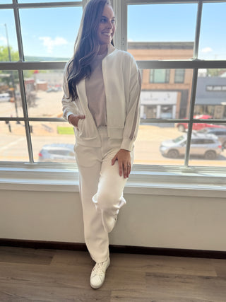 Photo of a woman wearing a white jacket and pants standing in front of a window.