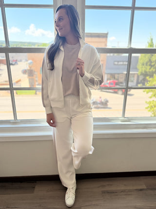 A woman in a white jacket and pants standing up against a window.
