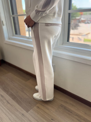 Person wearing a white outfit standing in a room with wooden flooring and a window.