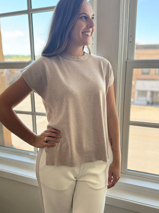 Photo of a woman standing in front of a window in a rosy taupe short sleeve top.