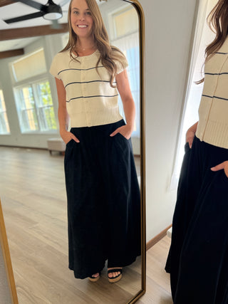 Woman wearing a cream sweater with black stripes and dark blue pants, standing in front of a mirror.