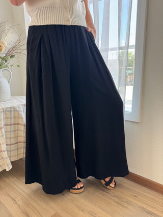 Person wearing a white top and black wide-leg pants indoors.