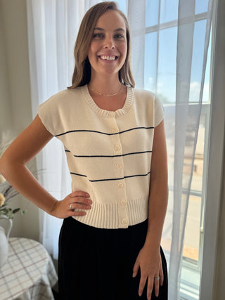 Woman wearing a cream-colored striped sweater in a bright room with large windows.
