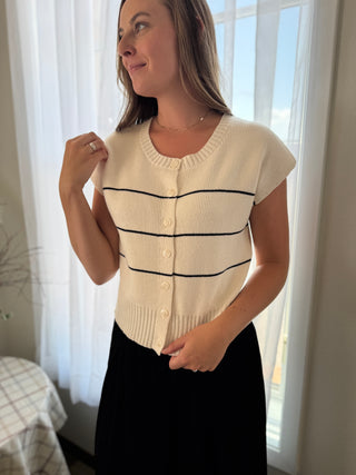 Woman wearing a cream-colored cardigan with black stripes indoors.