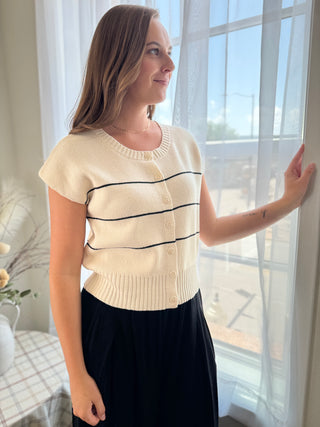 Woman wearing a cream-colored sweater with black stripes indoors by a window.