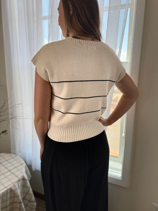 Woman wearing a cream sweater with black stripes in a room with white curtains.