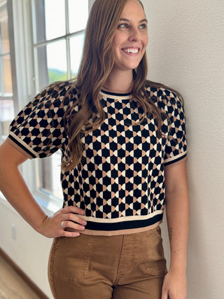 Lady looking out window wearing a checkered top with banded sleeves and waist.
