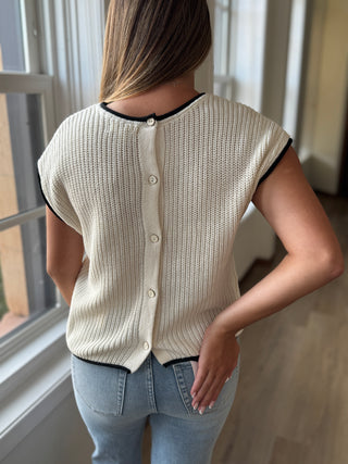 Person wearing a cream-colored knit cardigan with black trim in a room with a window.
