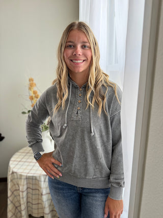 Woman wearing a gray hoodie and jeans standing indoors.