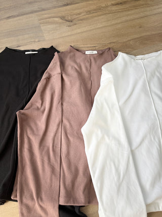 Three shirts in black, brown, and white on a wooden surface
