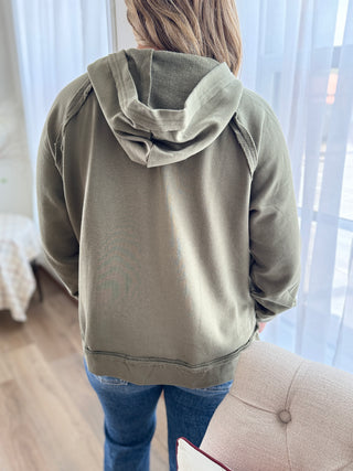 Person wearing a green hoodie in a room with curtains and furniture.