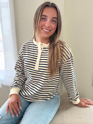 Woman wearing a striped shirt sitting on a couch with a neutral background