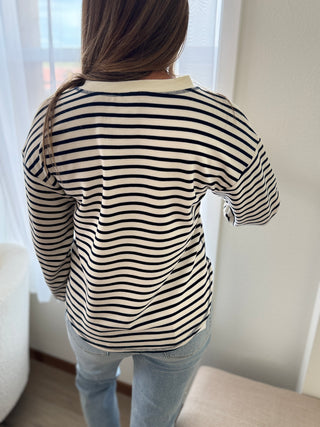 Person wearing a black and white striped shirt in a room with a white curtain.