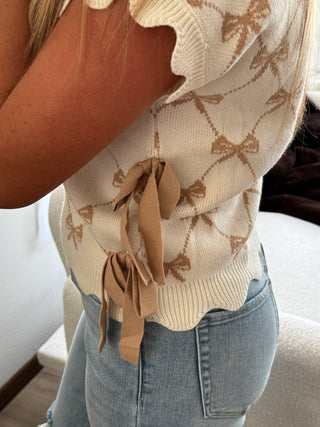 Close-up of a person wearing a beige patterned sweater with brown ribbons and blue jeans.